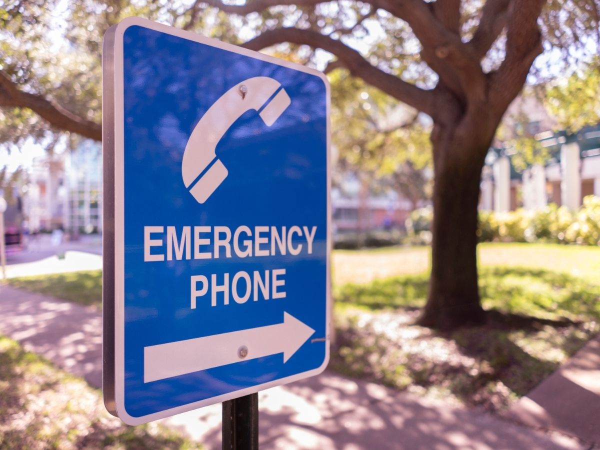 A blue and white outdoor sign with a photo of a phone, an arrow and the words "Emergency Phone"